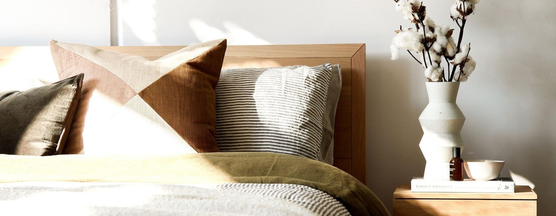 swath of sunlight shines across a well made bed and bedside table with a vase of cotton plants